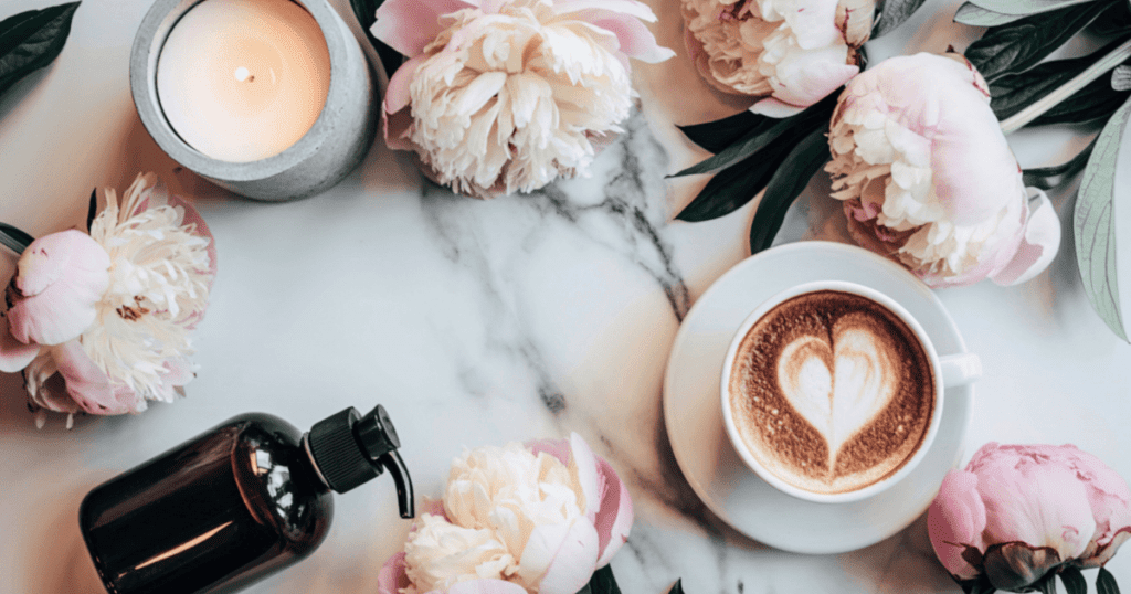 Cappuccino mit Herz-Latte-Art auf Marmortisch, Kerze und Pfingstrosen · ruhige, warme Stimmung