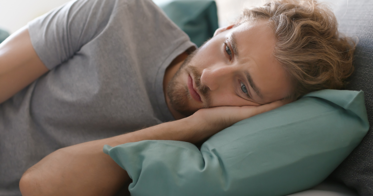 Junger Mann liegt wach im Bett und wirkt nachdenklich und belastet.